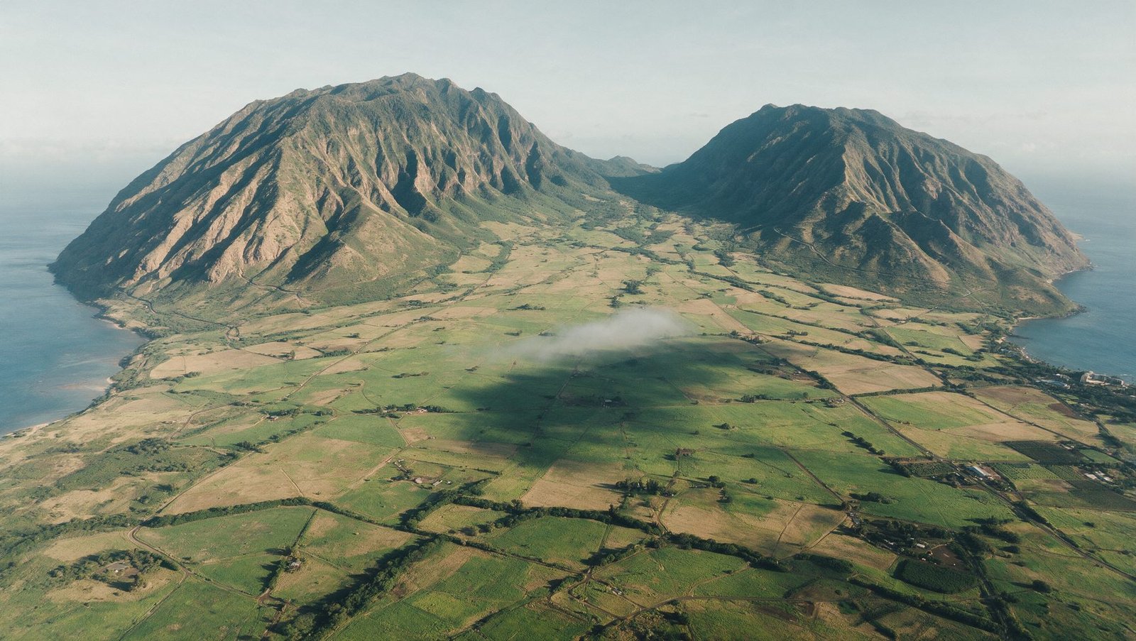 Aerial view across the green central Maui isthmus with the West Maui mountains rising on one side and the ocean on both